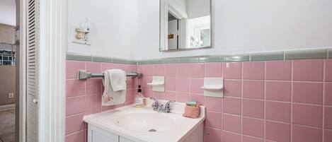 A bathroom with a white sink, pink tiles, a towel rack, a mirror, and a soap dispenser.