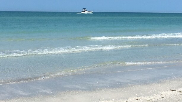 Una playa con agua cristalina y un barco a lo lejos.