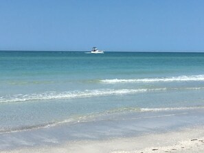Ein Strand mit klarem Wasser und einem Boot in der Ferne.