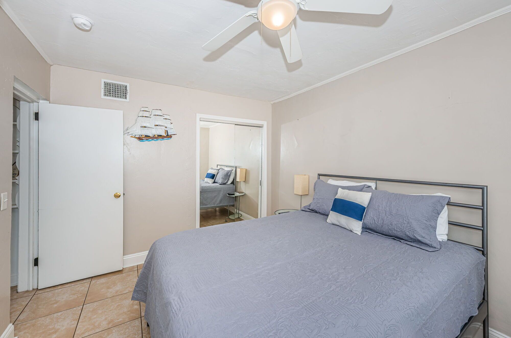 A bedroom with a bed, a ceiling fan, a door, and a mirror.