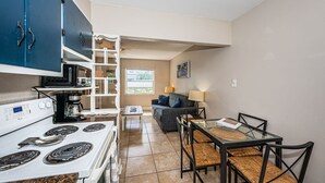 Cocina compacta con estufa, microondas y armarios. Hay una zona de comedor con mesa y sillas.