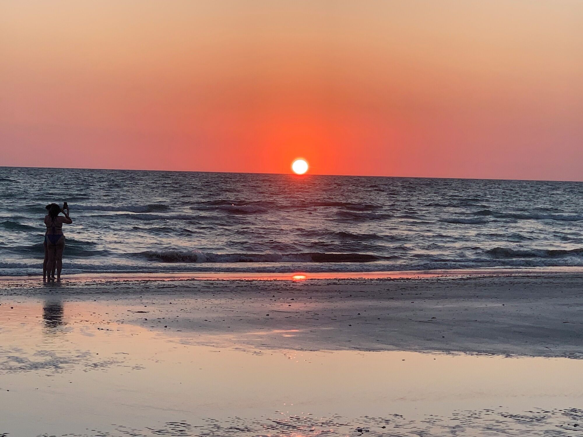 A sunset over the ocean with a person taking a photo.