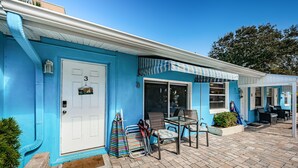 Una casa azul con una puerta blanca, un pequeño porche con sillas y una ventana.