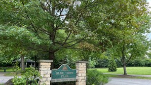 A sign for Olde Town Park with a stone archway, surrounded by lush greenery and trees. - "The Owl's Nest" Updated Craftsman home overlooking Old Town Park. (Westerville)
