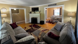 A living room with a fireplace, a dining area, and a clock on the wall. - "The Owl's Nest" Updated Craftsman home overlooking Old Town Park. (Westerville)