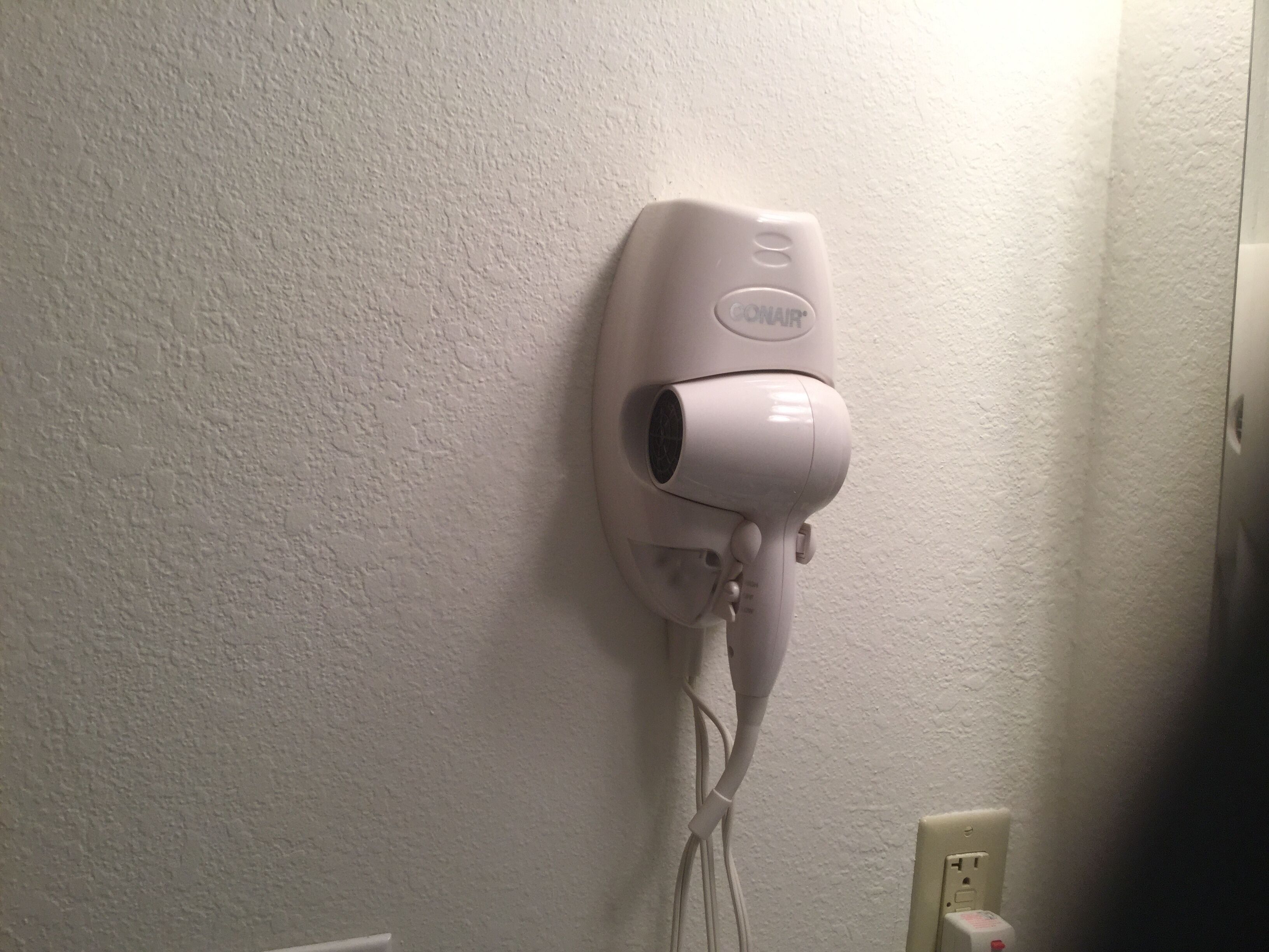 A hair dryer mounted on a textured wall, connected to a power outlet.