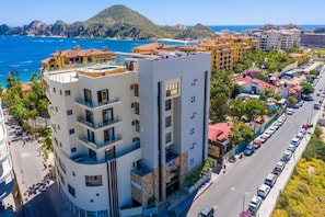 A multi-story hotel with balconies overlooking a coastal area, a parking lot, and a view of the sea and mountains. - Medano Beach, Ocean View, Downtown, 3BD, 6th floor (Cabo San Lucas)