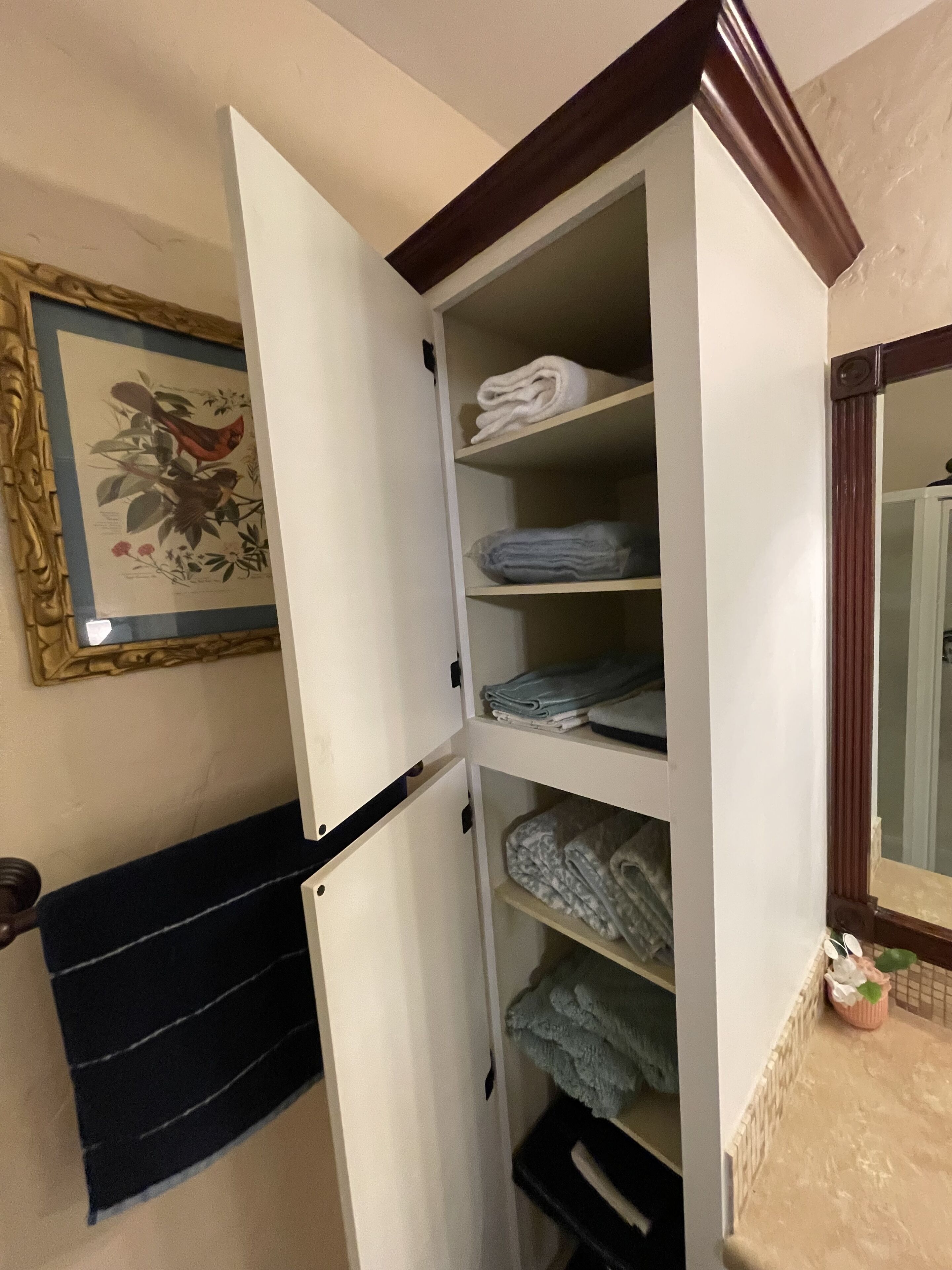 Ein Zimmer mit integriertem Kleiderschrank, der mehrere Ablagen für gefaltete Kleidung bietet, einer schwarzen Bank und einem gerahmten Pflanzenprint an der Wand.