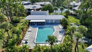 An aerial view of a resort with a swimming pool surrounded by lounge chairs and palm trees.