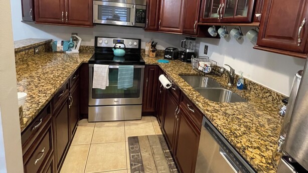 A modern kitchen with dark wooden cabinets, granite countertops, stainless steel appliances, and a built-in microwave.
