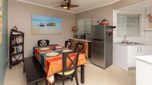 Cocina compacta con refrigerador, microondas y lavamanos. Hay una zona de comedor con mesa y sillas, y un ventilador de techo.
