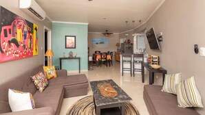 Una sala de estar con un sofá, una mesa de centro y un televisor. Hay una zona de comedor con sillas y una mesa.