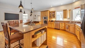 A modern kitchen with wooden cabinets, a central island, and pendant lighting. - BigBear Lodge: Mt. Sunapee / Hot tub / Firepit (New London)