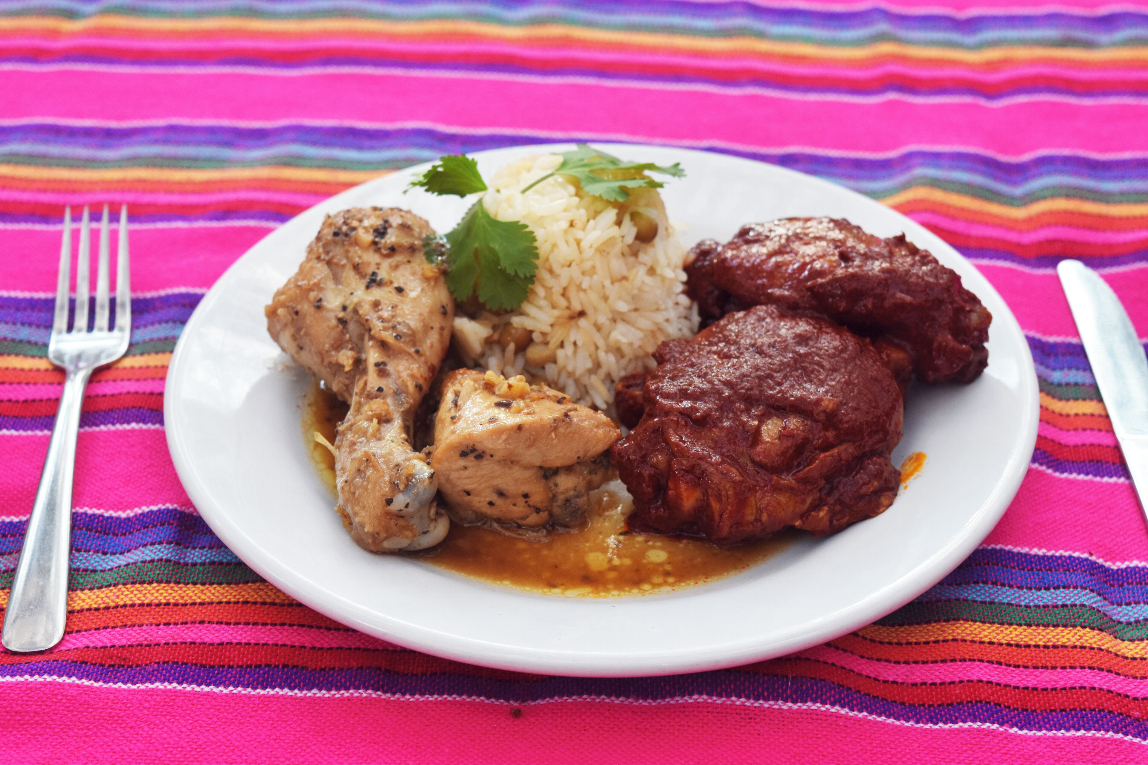 Un plato de comida con arroz, pollo y un guiso de carne, sobre un mantel a rayas de colores.
