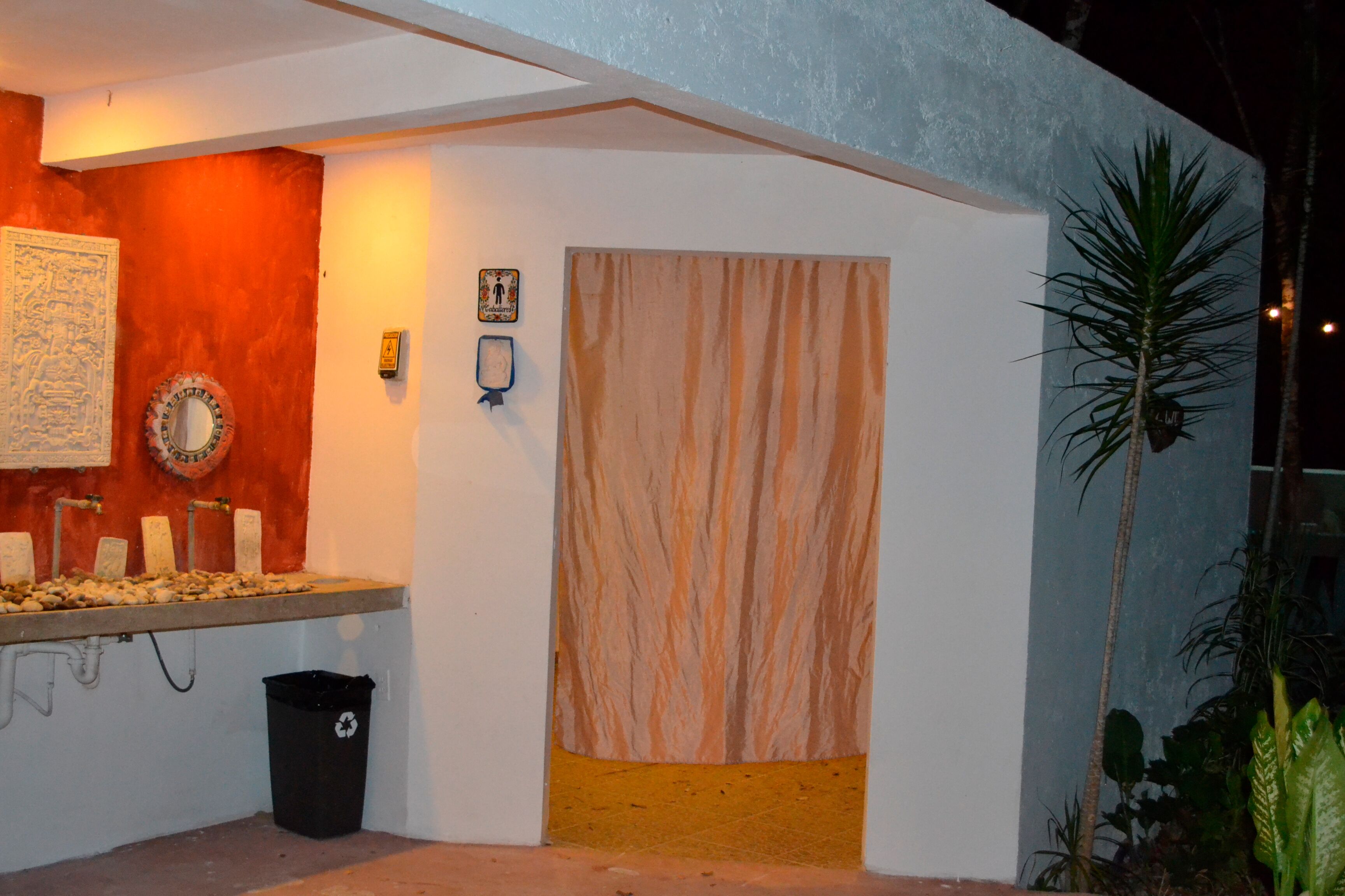 A bathroom with a sink, mirror, and towel rack. There is a trash bin and a towel hanging on the wall.