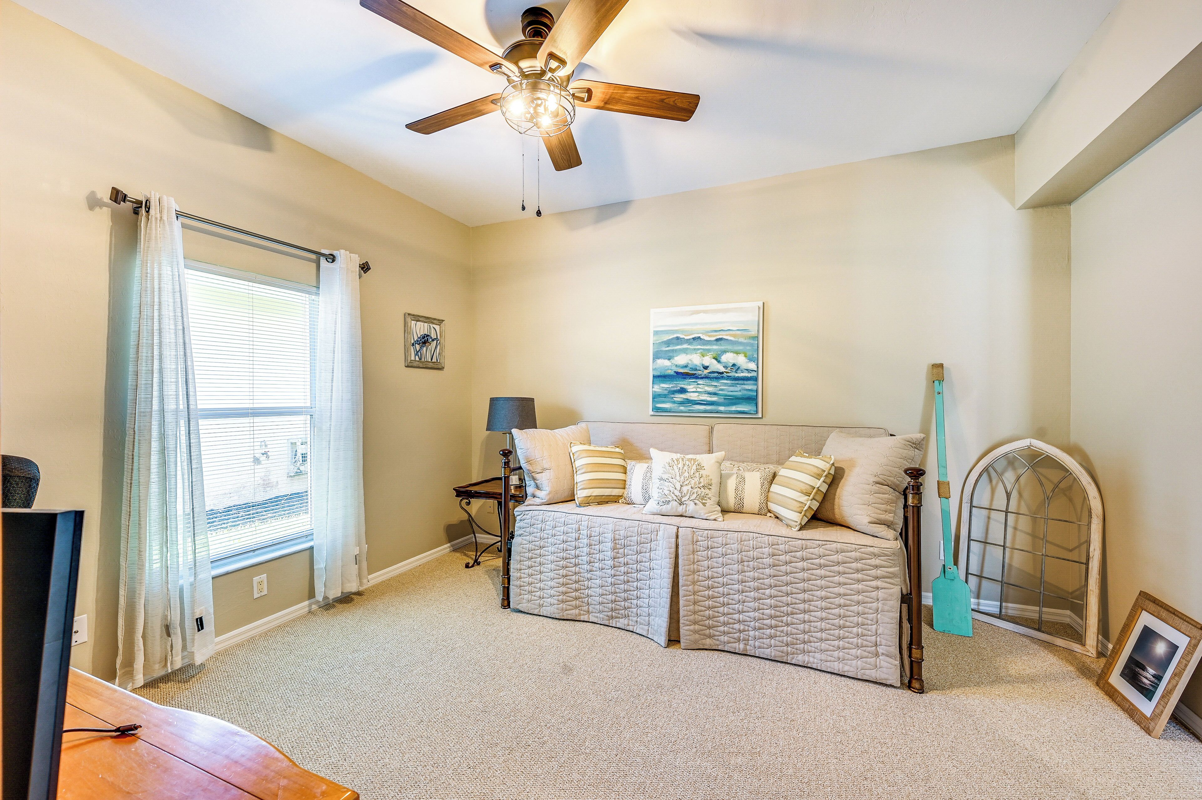 A bedroom with a bed, a ceiling fan, a window with curtains, a lamp, and a picture frame on the floor.