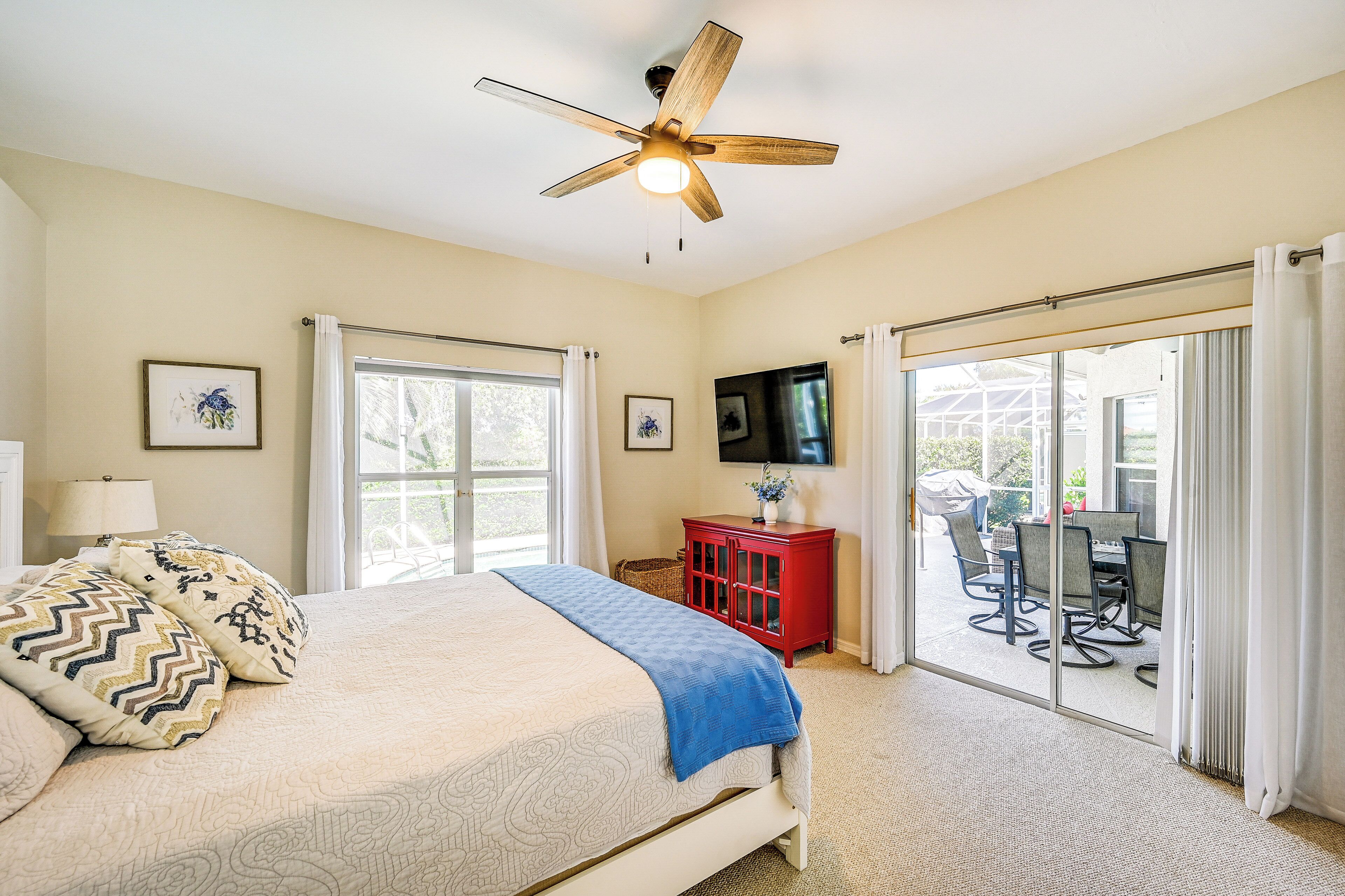 A bedroom with a bed, a ceiling fan, a TV, and a sliding glass door leading to an outdoor area.