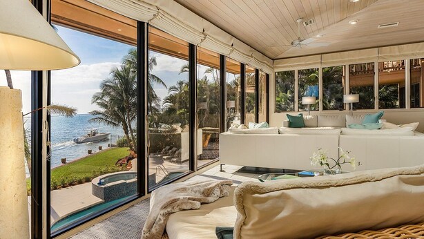 Una sala de estar moderna con un amplio ventanal que da a una piscina y al mar.
