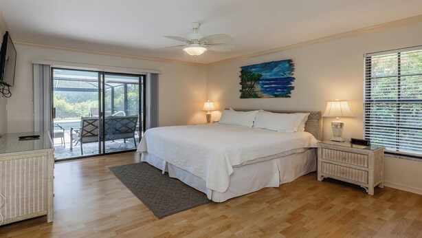 A bedroom with a bed, a nightstand, a desk, a chair, a window with blinds, and a ceiling fan. - Lovely three-bedroom two-bathroom with pool and spa, and a short distance to Tigertail (Marco Island)