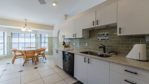 A modern kitchen with white cabinets, a dishwasher, a sink, and a dining area with wicker chairs. - Lovely three-bedroom two-bathroom with pool and spa, and a short distance to Tigertail (Marco Island)