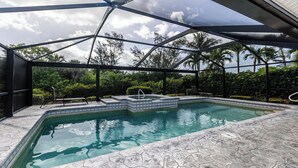A swimming pool with a hot tub, surrounded by a covered area with chairs and a view of palm trees. - Lovely three-bedroom two-bathroom with pool and spa, and a short distance to Tigertail (Marco Island)