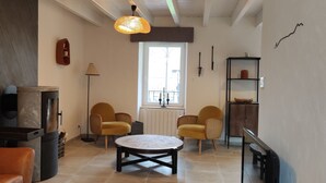 Een woonkamer met een open haard, twee gele fauteuils, een ronde salontafel en een groot raam.