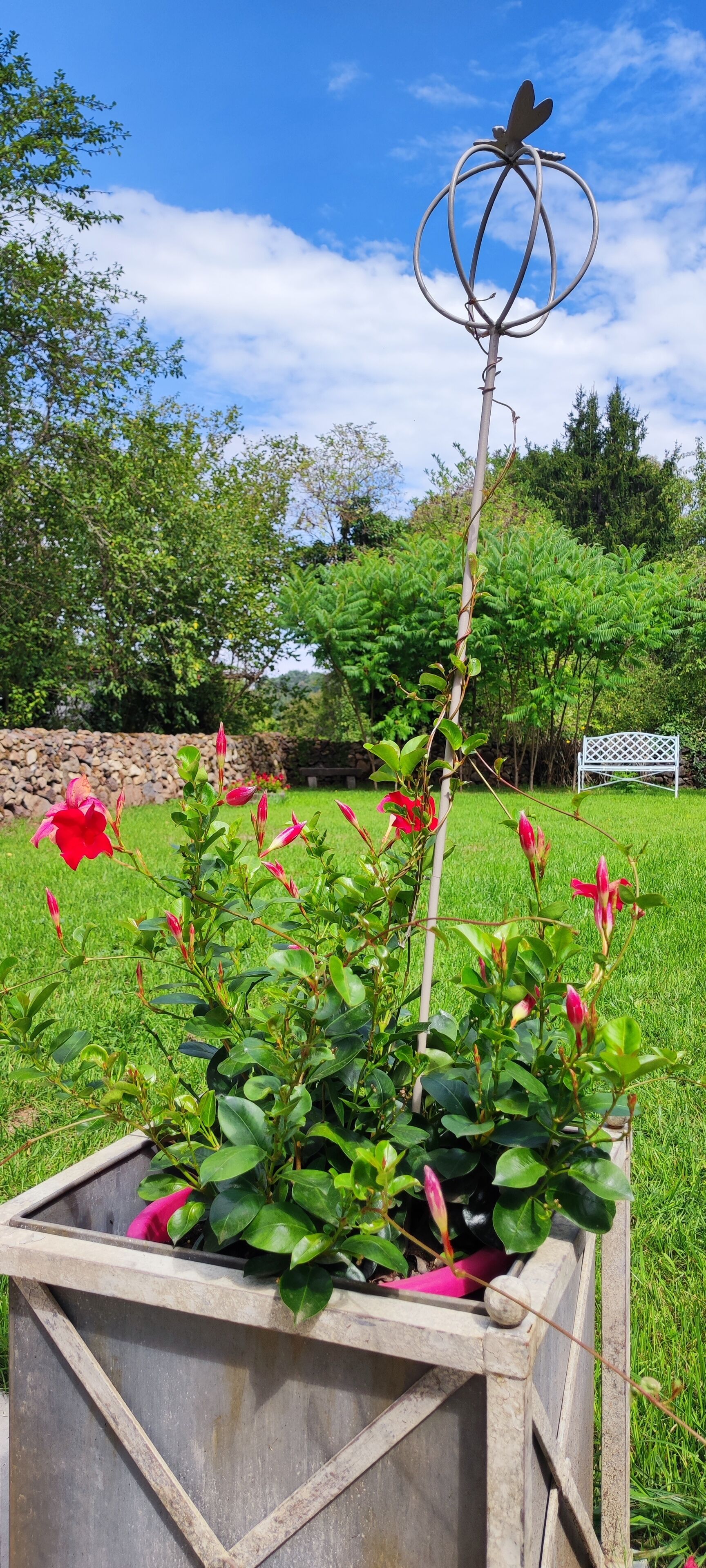 A garden with a metal sculpture, a planter box, and a stone wall in the background.