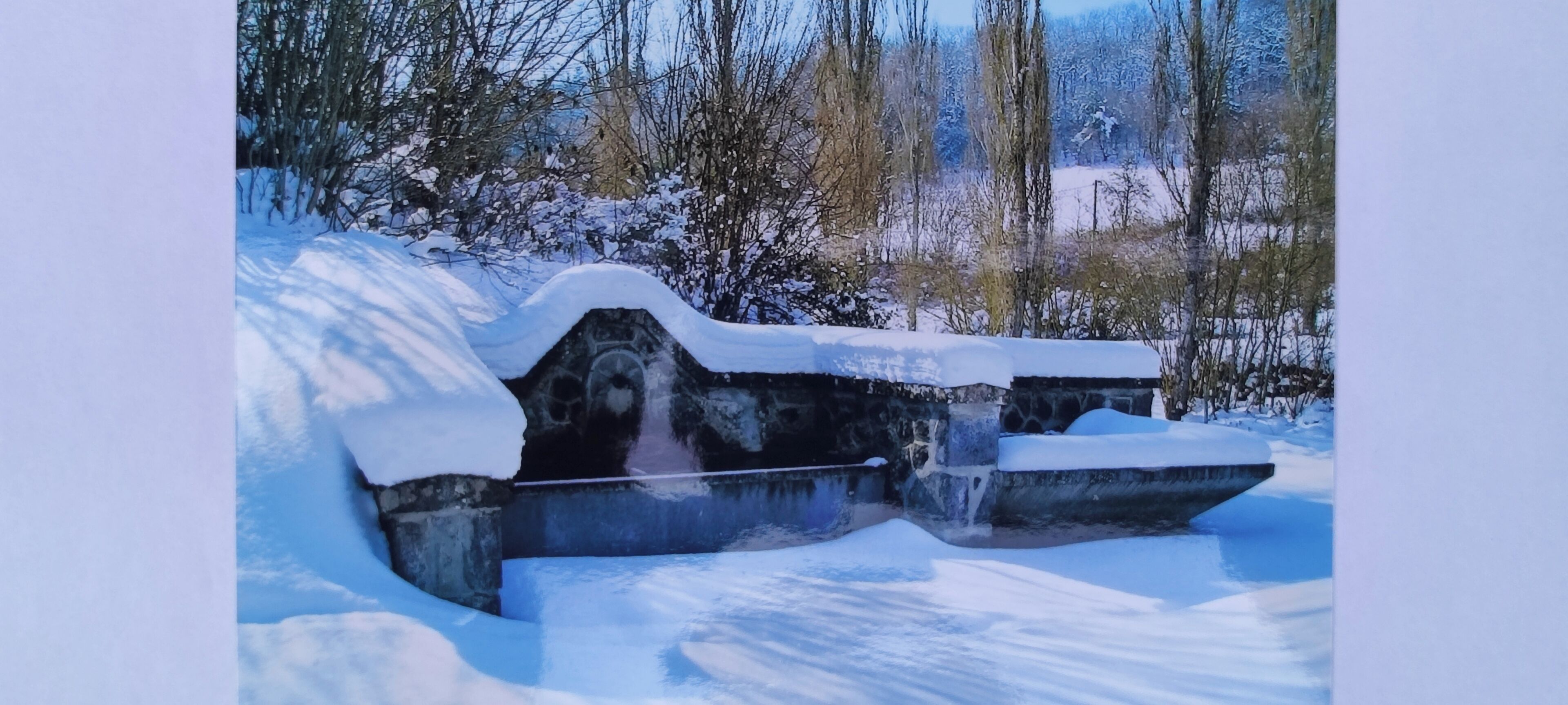 Eine steinerne Struktur, teilweise mit Schnee bedeckt, inmitten einer verschneiten Landschaft und Bäumen.