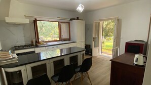 Cocina compacta con una isla central, comedor con sillas y vista a un espacio exterior por una puerta corrediza de vidrio.