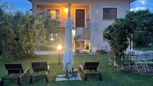 Una casa de dos pisos con un balcón, una zona de estar al aire libre techada y un jardín cuidado.