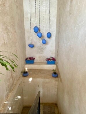 A narrow corridor with a tiled floor, a metal railing, and blue hanging planters with flowers. - Casa Caribe Tulum (Tulum)
