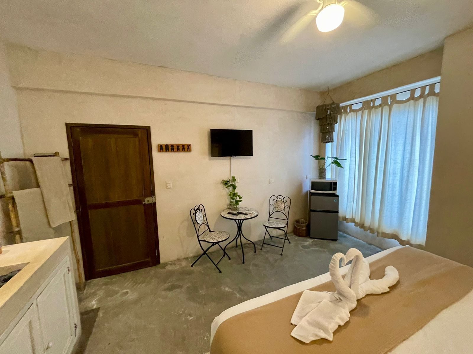 Habitación de hotel con cama, escritorio, dos sillas, televisión y una pequeña mesa con una planta.