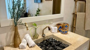 A bathroom with a beige sink, a mirror, a plant, towels, and decorative wooden containers. - Casa Caribe Tulum (Tulum)