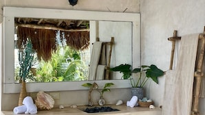 A bathroom with a large mirror, a wooden vanity, a hanging light fixture, and a view of the outdoors through the window. - Casa Caribe Tulum (Tulum)