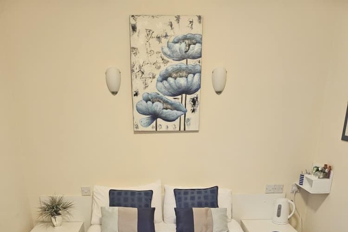 A bedroom with a bed, two bedside tables, a wall-mounted artwork, and a small shelf with items.