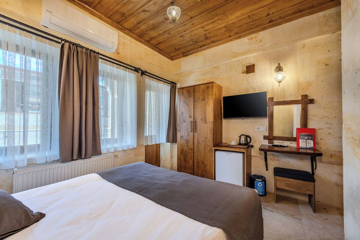 A bedroom with a bed, a wooden wardrobe, a small desk with a mirror, a television, and a radiator.
