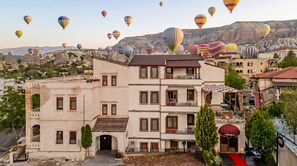 A multi-story building with balconies, a red carpet entrance, and a view of hot air balloons in the background. - Rocca Stone House (Nevsehir)