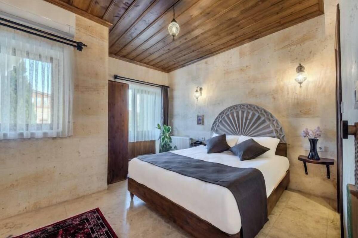 A bedroom with a bed, wooden ceiling, wall sconces, and a door.