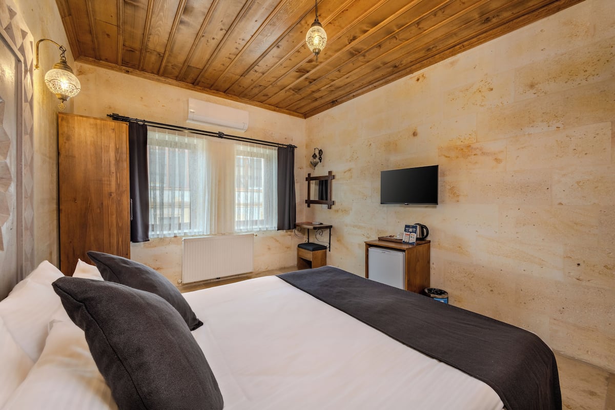 A bedroom with a bed, a television, a small table, and a window with curtains.