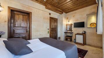 Habitación de hotel con techo de madera, cama con ropa de cama gris, televisor, mesita con tetera y televisor montado en la pared.