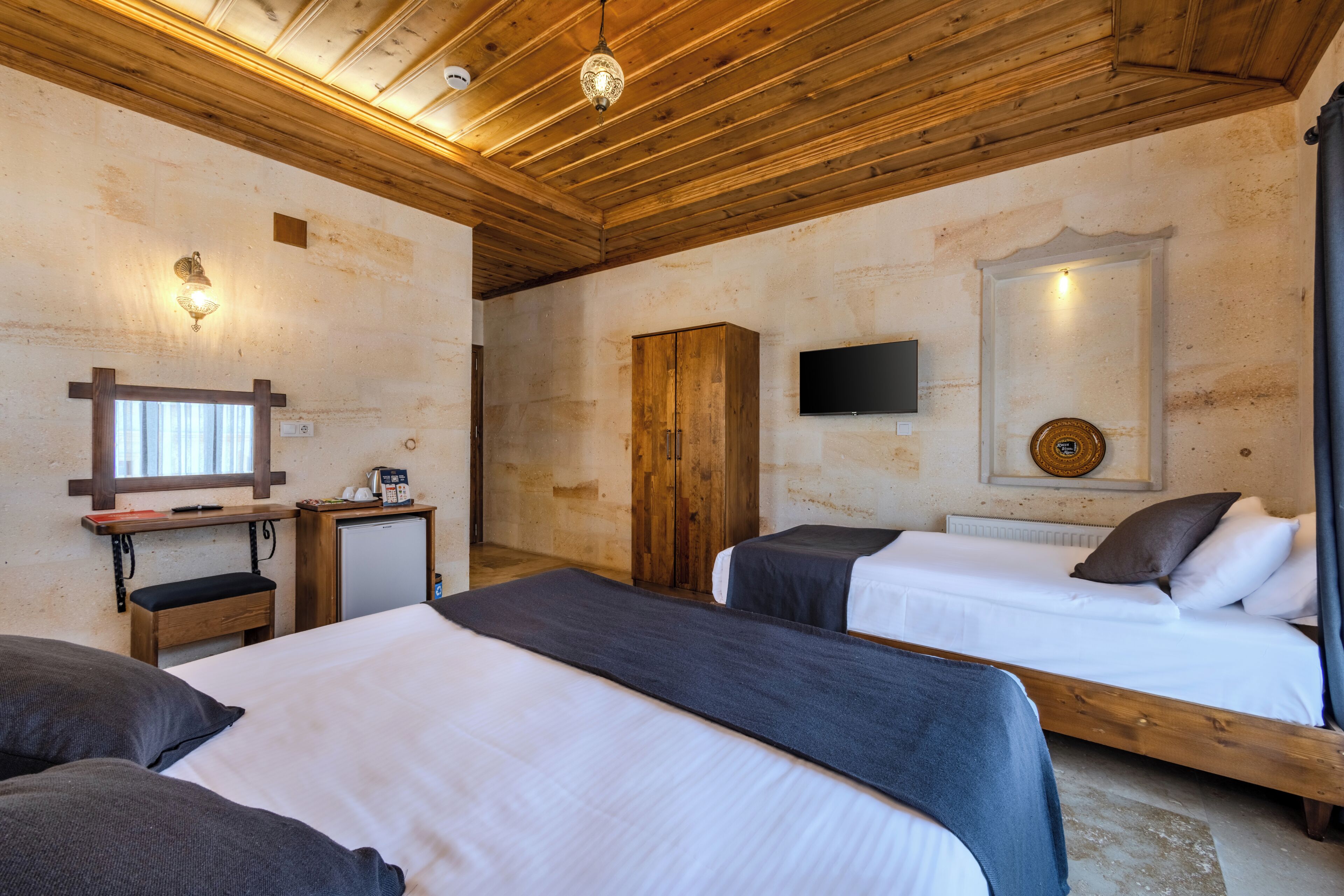 Una habitación con dos camas, techo de madera, televisor y un pequeño escritorio con teléfono.