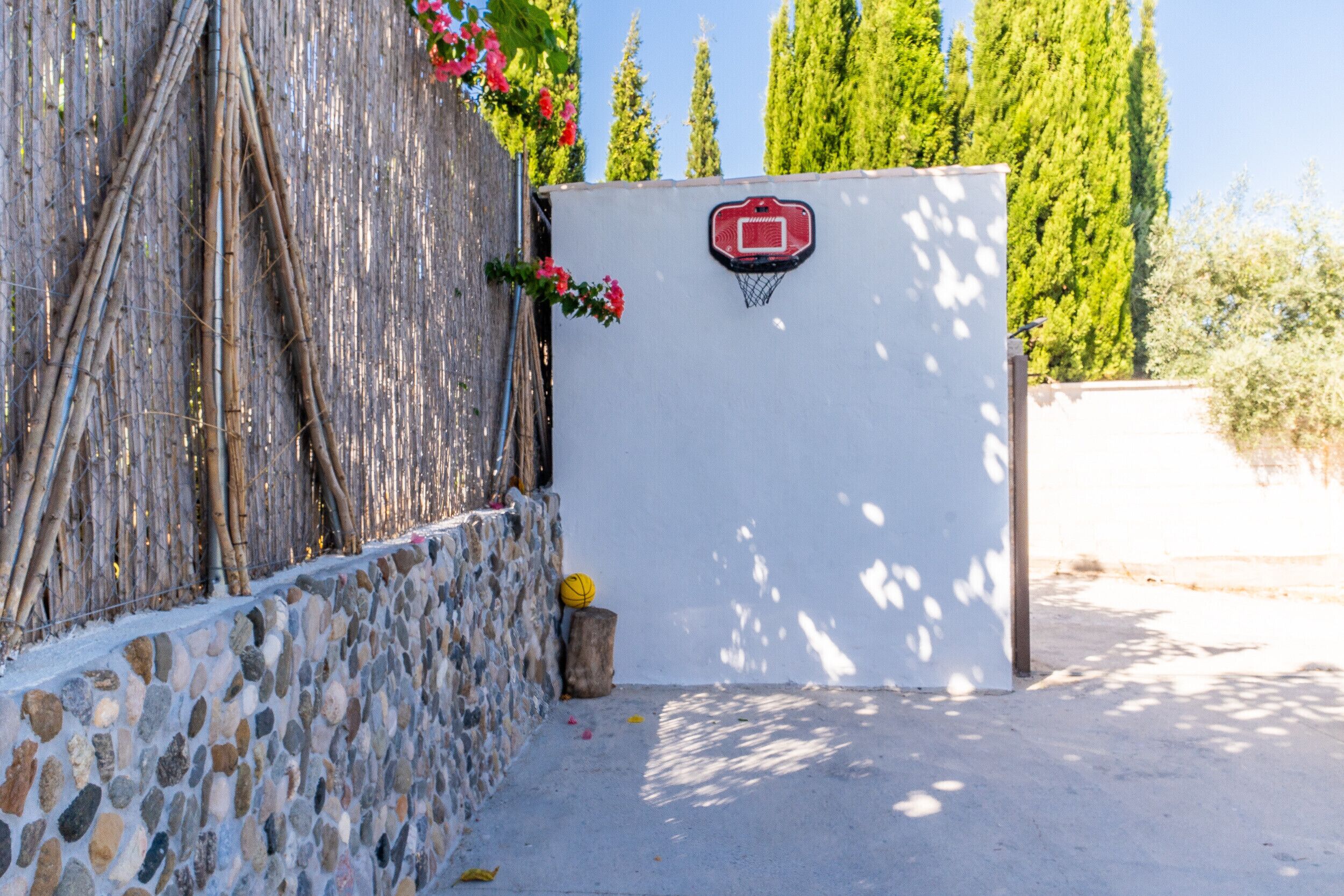 Un panier de basket avec un panneau arrière rouge, un mur en pierre et une clôture en bois.
