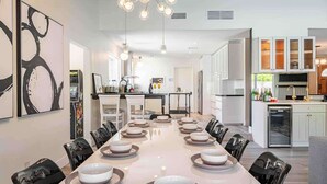 A modern kitchen with white cabinets, a dining area with a long table set for six, and a chandelier. - Paramount Palm Springs: An Enchanting Hollywood (Palm Springs)
