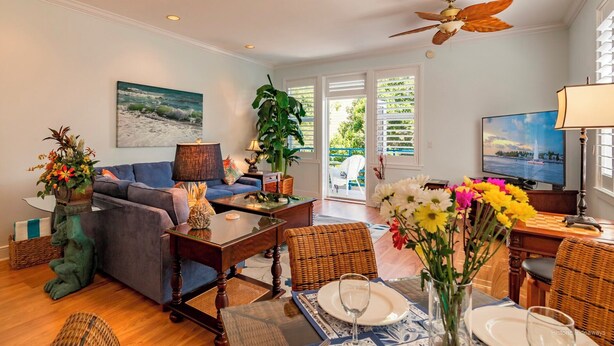 A spacious living room with a blue sofa, a dining area with a table set for two, and a large window with a view of the outdoors. - Banana Key (Key West)