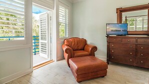 A room with a brown leather armchair and ottoman, a wooden dresser, and a television on top. - Banana Key (Key West)