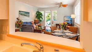 A modern kitchen with a large island, dining area with wicker chairs, and a view of the outdoors through large windows. - Banana Key (Key West)