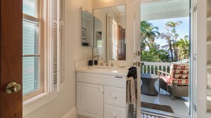 Une salle de bain avec un meuble-lavabo blanc, un grand miroir et une vue sur un balcon aménagé avec du mobilier d’extérieur.