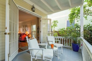 A covered porch with white wicker furniture, a glass table, and a potted plant.