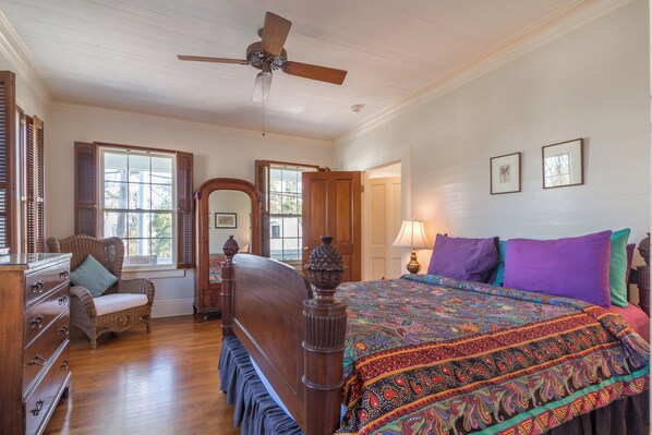 A bedroom with a wooden bed, a ceiling fan, a window with shutters, and a dresser.