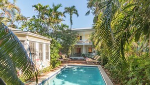 Une piscine entourée d’une végétation luxuriante et un bâtiment doté d’un balcon.